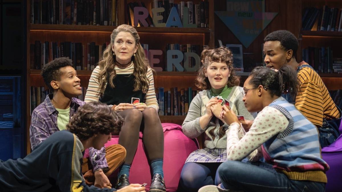 Older woman holding uno cards while several children sit around her on beanbags in a library also holding uno cards